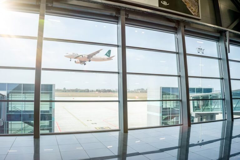 An aircraft taking off beyond the glass windows of an airport terminal.