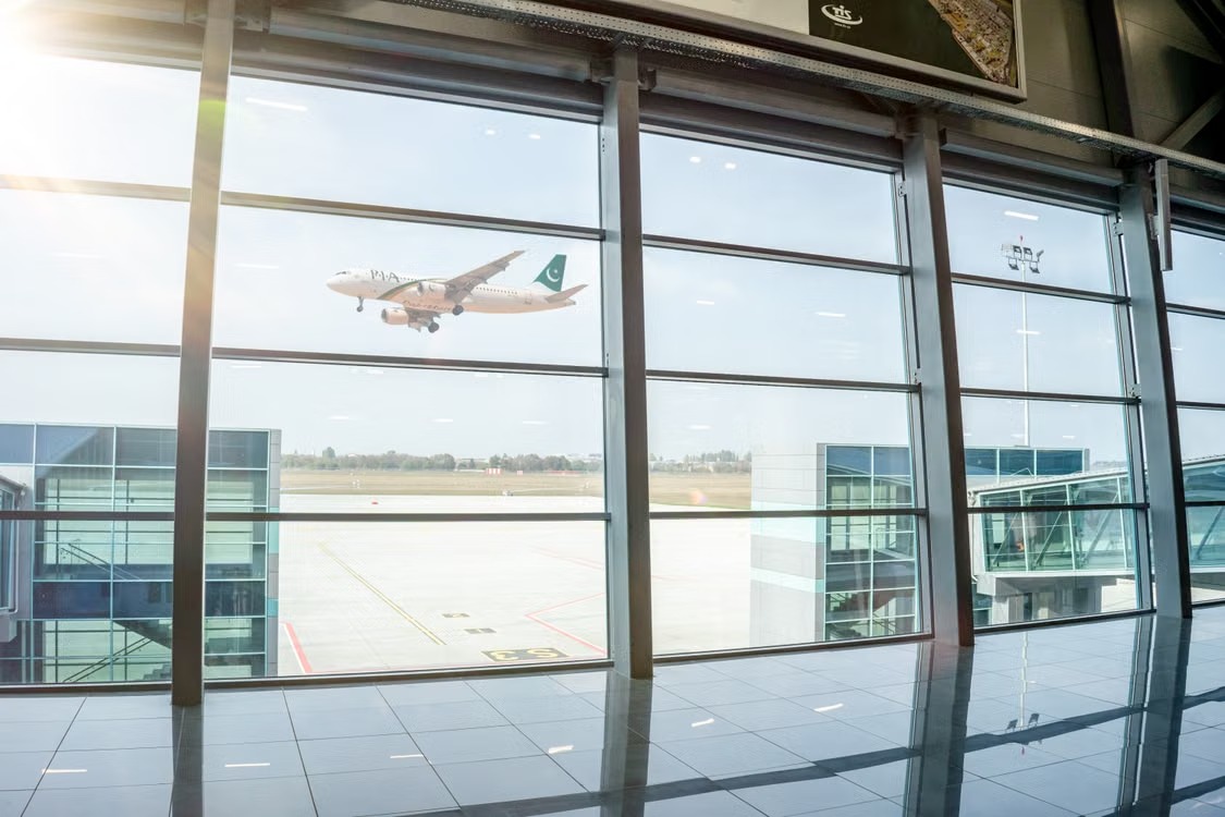 An aircraft taking off beyond the glass windows of an airport terminal.